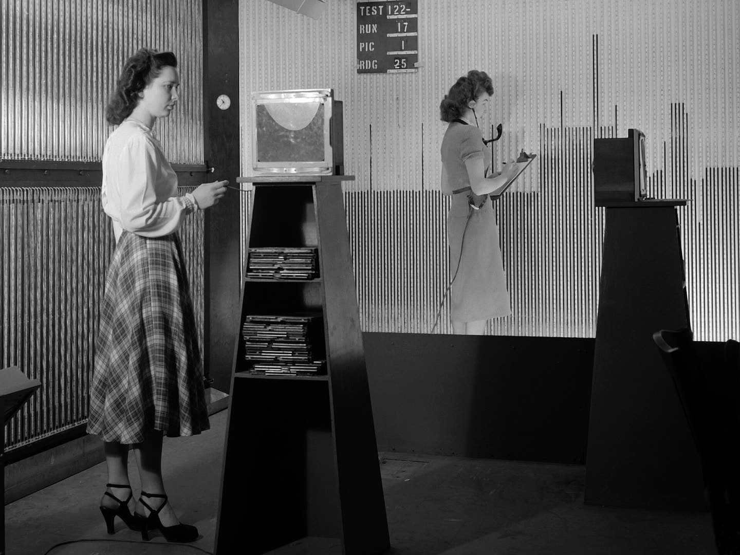 Two women in 1949 reading rows of manometer tubes, under a board marked test 122, run 17, picture 1, reading 25
